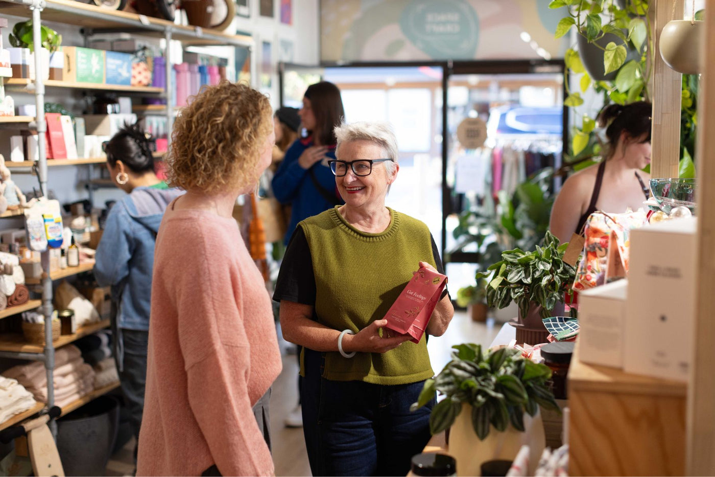 Woman holding a red packet in a store with other people and shelves in the background